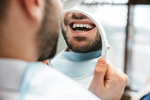 Nose-down image of man smiling at his reflection in handheld mirror